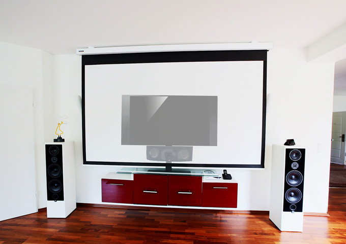 Im Wohnzimmer muss nichts mehr umgestellt werden, wenn ein Film auf der Großbildwand geschaut werden soll. Die Motorleinwand wird dafür über dem TV-Gerät angebracht. Für den Start des Filmabends oder die Fußball WM reicht ein Knopfdruck. Die Leinwand wird so weit herunter gefahren, bis sie ihre optimale Position erreicht hat. Der Centerlautsprecher und das TV-Gerät verschwinden dahinter. Nun kann der Center problemlos durch die schalldurchlässige Leinwand tönen. Foto: Michael B. Rehders