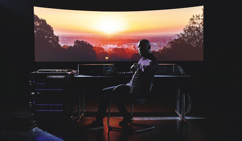 Canon Ambassador und Explorer Simeon Quarrie mit zwei Canon 4K500ST Installationsprojektoren und einem Wings Engine Raw Server von AV Stumpfl vor der Projektionsleinwand.