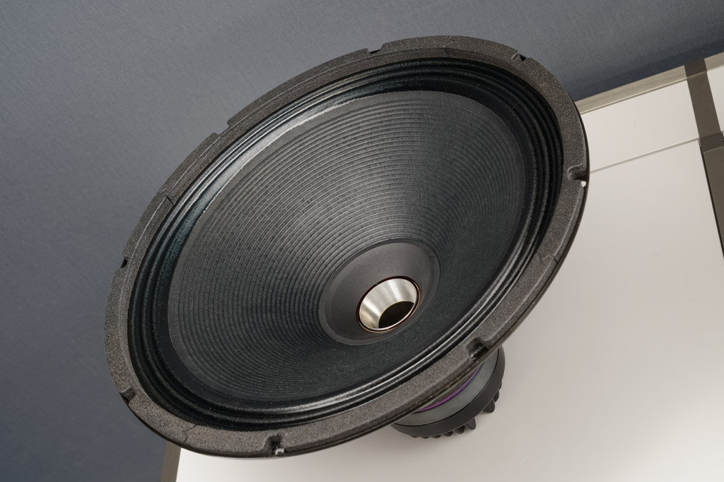 Hier ist das zuoberst sitzende Koaxial-Chassis ausgebaut und damit sichtbar: Die Höhen und Mitten bis 800 Hertz liefert ein Tweeter, der seinen Schall über einen Tunnel zentral durch den Antrieb des Woofer abstrahlt. Wir sehen das Ende dieses Tunnels, er mündet in eine zweiteilige Schallführung: Der silbermetallene Hornansatz ist dabei starr und fest, die schwarze Schallführung hingegen wurde auf die Konusmembran des Mitteltieftöners aufgeklebt. Dieses Präzisionsteil aus superleichtem und überaus steifem Polyamid wird von Mach One classics im 3D-Druck-Verfahren gefertigt.