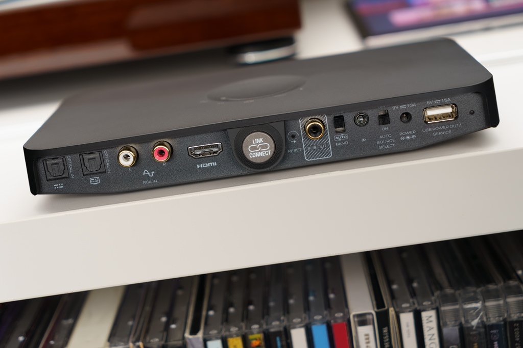 Der Sound Hub Compact bietet zum Anschluss von Zuspielern und Quellen zwei digitale optische Inputs, einen analogen Line-Eingang und eine HDMI-Schnittstelle. Der „Link Connect“-Taster dient dem komfortablen Paaren mit den Lautsprechern. Falls man kompakte Schallwandler wie die Callisto 2 C, die Rubicon 2 C, die Oberon 1 C oder die Oberon On-Wall C wählt, lohnt sich für einen kraftvolleren und tieferen Bass der Anschluss eines aktiven Subwoofers an dem „Sub Out“. Mit dem „Band“-Schalter ändert man den Funkfrequenzbereich, in dem der Hub seine Signale an die verbundenen Lautsprecher sendet. Die Standard-Einstellung ist 5,8 Gigahertz, in der „Auto Band“-Einstellung hingegen wechselt der Hub je nach Auslastung des WLAN in das 5,2 Gigahertz-Band. An die IR-Buchse schließt man den mitgelieferten externen Infrarot-Empfänger an, falls der Hub keine freie „Sicht“ zur Fernbedienung hat. Bei aktiviertem „Auto Select“ schalten sich der Hub und die Lautsprecher automatisch an, sobald eine Quelle ein Signal sendet, und wechseln zugleich auf diesen Eingang. Die Stromversorgung des Hubs geschieht über ein externes Steckernetzteil, das an die „Power“-Buchse angeschlossen wird. Der Hub wiederum kann über seinen USB A-Port ein zuspielendes Smartphone oder Tablet mit Strom versorgen.