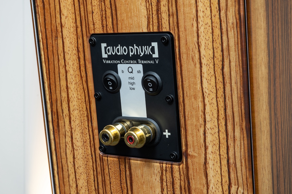 Das Anschlussfeld der Cardeas: Hier finden wir, neben den höchstwertige WBT-Klemmen aus der nextgen-Serie, auch auch die Kippschalter für die Bassanpassung. Das gesamte Terminal ist mehrfach vibrationsentkoppelt: Die Tafel ist rückseitig mit einer schwingungsabsorbierenden Gummischicht ausgestattet. Die Schrauben sind, wie wir es schon bei den Chassis gesehen haben, in Kunststoffdübel eingedreht. Die beiden Klemmen sind über eine elastische Kunststoffeinfassung von der Platte entkoppelt.