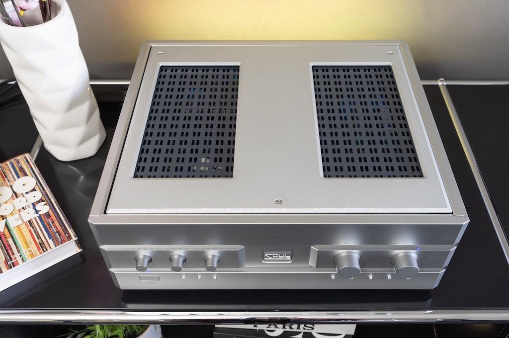 Die Oberseite des Gehäuses besteht aus einer zweiteiligen Metallplatten-Lösung. Sie liegt nur an drei Punkten definiert auf dem Gehäuse auf. Dieser unbefestigte Deckel wird allein durch die einfassenden Schienen in Postion gehalten. So kann er frei schwingen – was die Offenheit und Räumlichkeit der Wiedergabe befördert. Das kann jeder nachvollziehen, der mal im Betrieb auf die Oberseite etwa sein Portemonnaie legt.