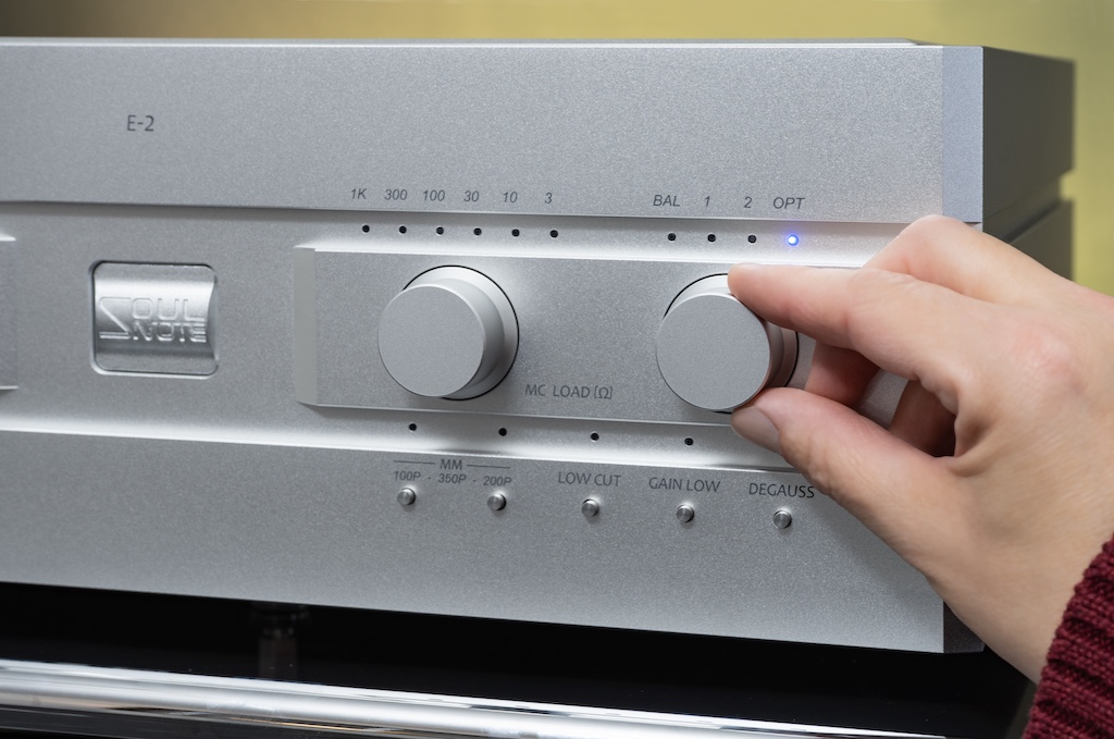 Der rechts betätigte Drehschalter dient der Eingangs-Wahl: Vier Inputs stehen zur Verfügung. Für MC-Systeme können sechs Impedanzwerte über den „MC Load“-Drehschalter eingestellt werden. Für MM-Abtaster stehen drei Kapazitätswerte zur Anpassung parat. Sie werden durch die zwei Druckschalter respektive ihre Kombination ausgewählt. Der „Low Cut“-Schalter senkt als Rumpelfilter tieffrequente Störgeräusche ab. Der „Low Gain“-Schalter verringert den hohen Ausgangspegel des E-2 um zehn Dezibel. Der „Degauss“-Schalter dient der Entmagnetisierung des Tonabnehmers.