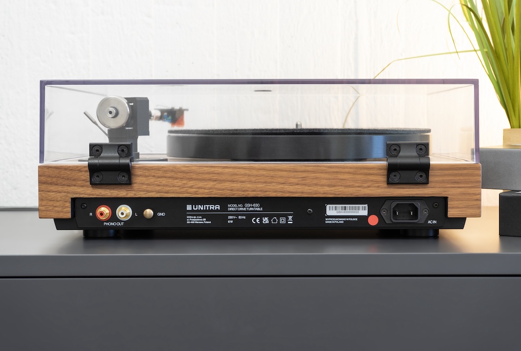 Auf der Rückseite finden wir links die Anschluss-Sektion mit vergoldeten Cinch-Buchsen und Erdungsklemme, rechts den Einbau-Netzstecker für die Stromversorgung des integrierten Netzteils. Die Phasenlage ist mit einem roten Punkt markiert.