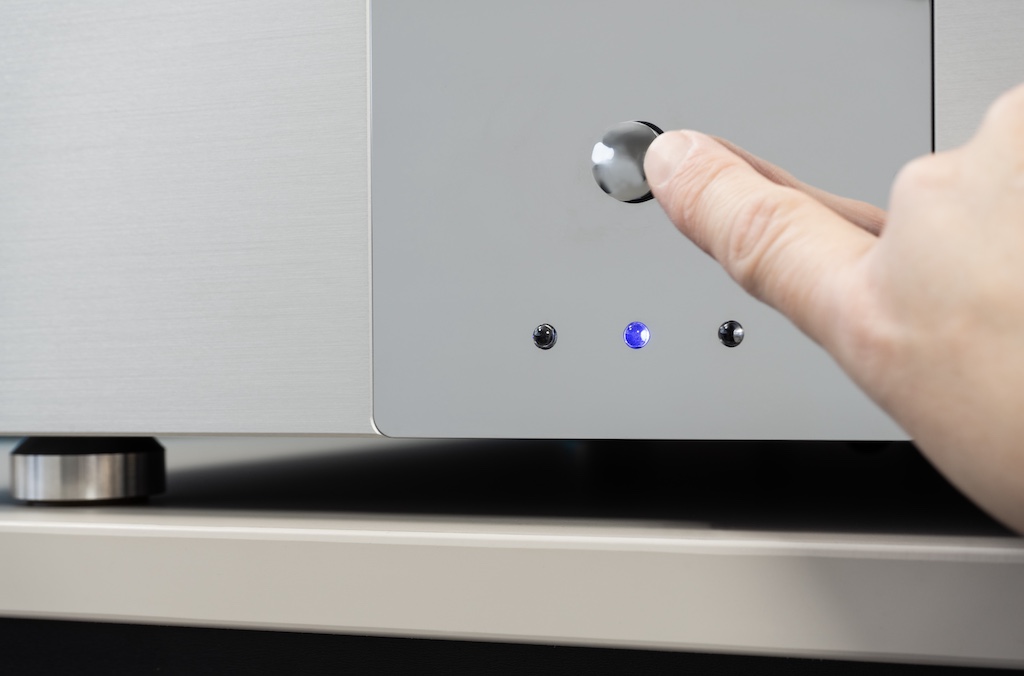 Die frontseitige Chromblende bietet als einziges Bedienelement den Ein/Aus-Druckschalter. Unter ihm geben drei LED Auskunft über den aktuellen Zustand der Stereo-Endstufe: Die blaue LED signalisiert die Betriebsbereitschaft, die beiden äußeren roten LED leuchten hingegen während des Aufwärm-Vorgangs. Sobald mit hörbarem und beruhigendem Relais-Klacken die Signalwege freigeschaltet werden, erlöschen diese LED. Leuchten sie währende des Betriebs, weisen sie auf eine Störung oder eine Verzerrung hin.